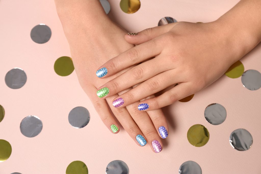 Woman showing her stylish colorful manicure on pink beige background, closeup
