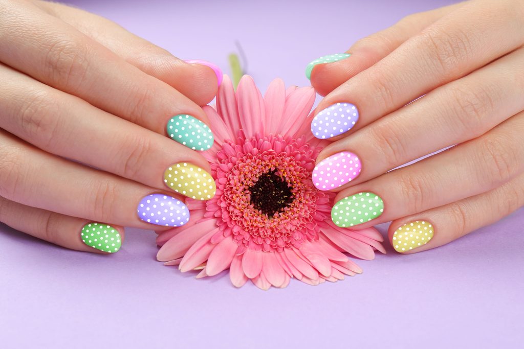 Woman with stylish colorful manicure holding gerbera flower on violet background, closeup
