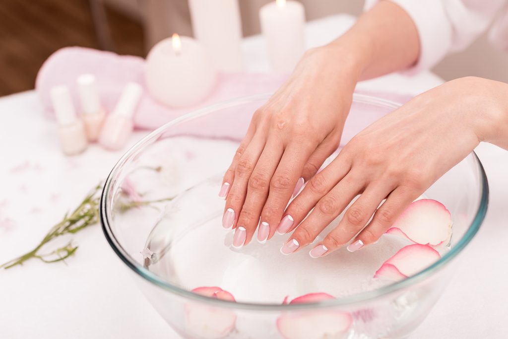 close-up view of female hands receiving spa treatment in glass bowl with rose . Removing Press-On Nails Safely at Home